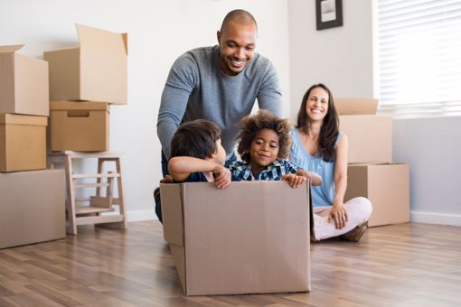 Un père afro-canadien heureux joue avec des enfants assis dans une boîte en carton dans leur nouvelle maison.