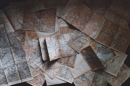 A large number of old maps (sepia colour) partially open to different degrees, all spread out and covering the table.
