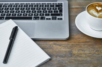 computer, pen, notepad and coffee on a table