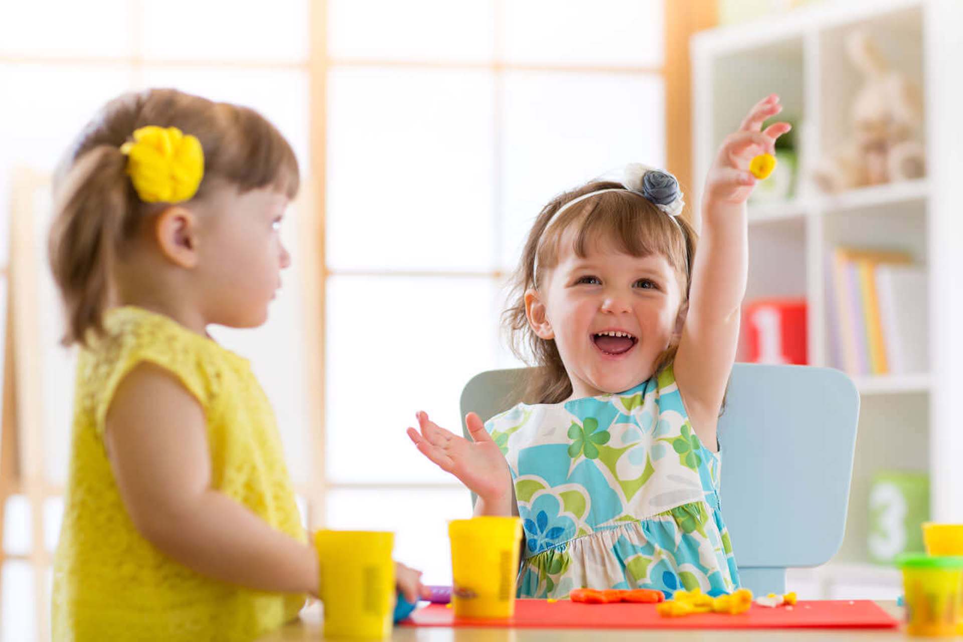 Two toddler aged girls in bright clothes playing together with Play-Doh.  Represents Children's Services for the feedback page.