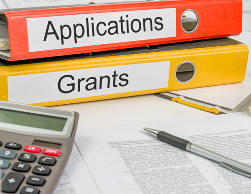 binders titled Applications and Grants with calculator, pen resting on top of a paper