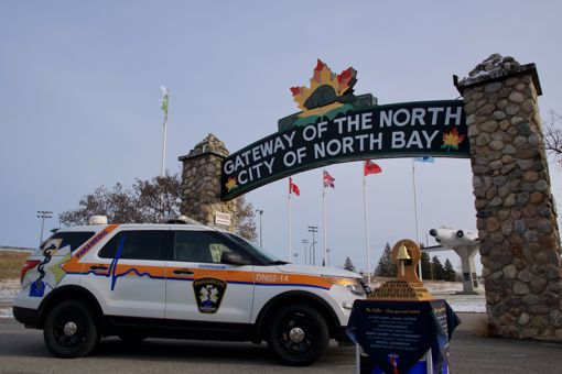The Paramedic Memorial Bell and one District of Nipissing Community Paramedic vehicles in front of the Gateway of the North Arch. 